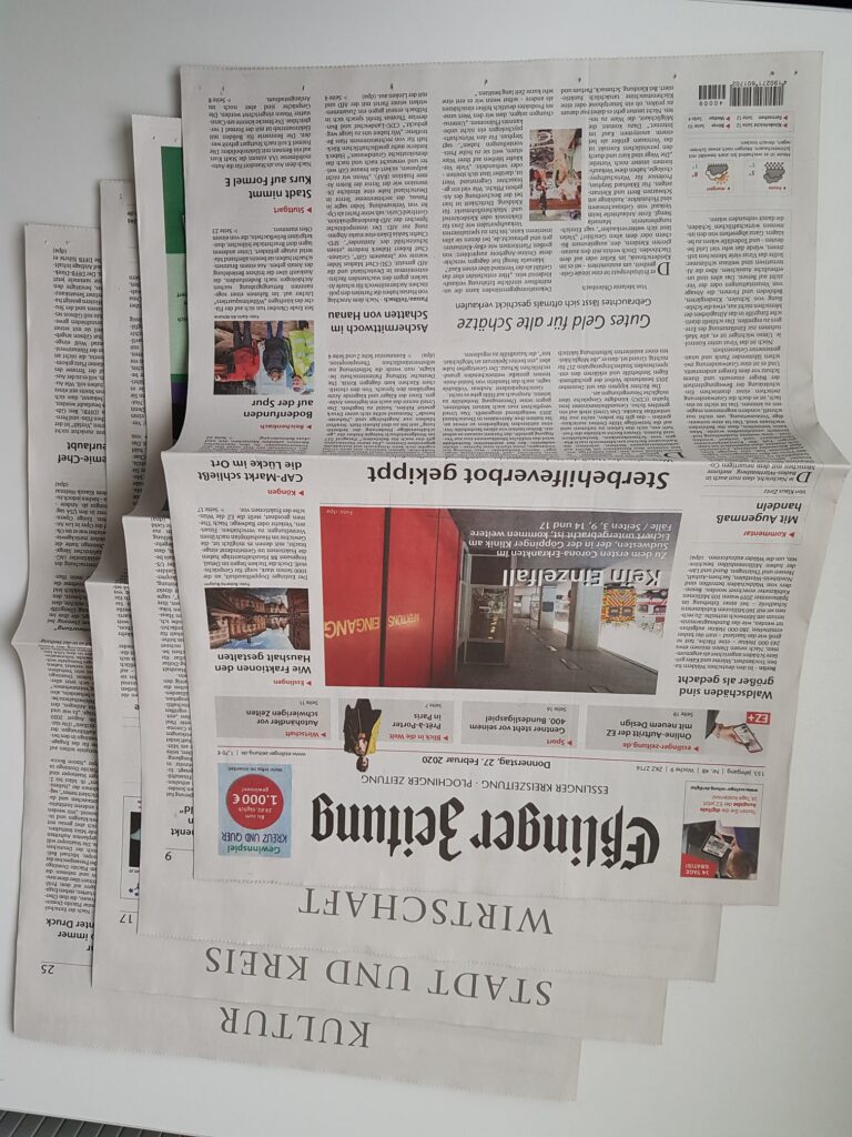 Zeitung im Vollformat mit hintereinander liegenden Büchern